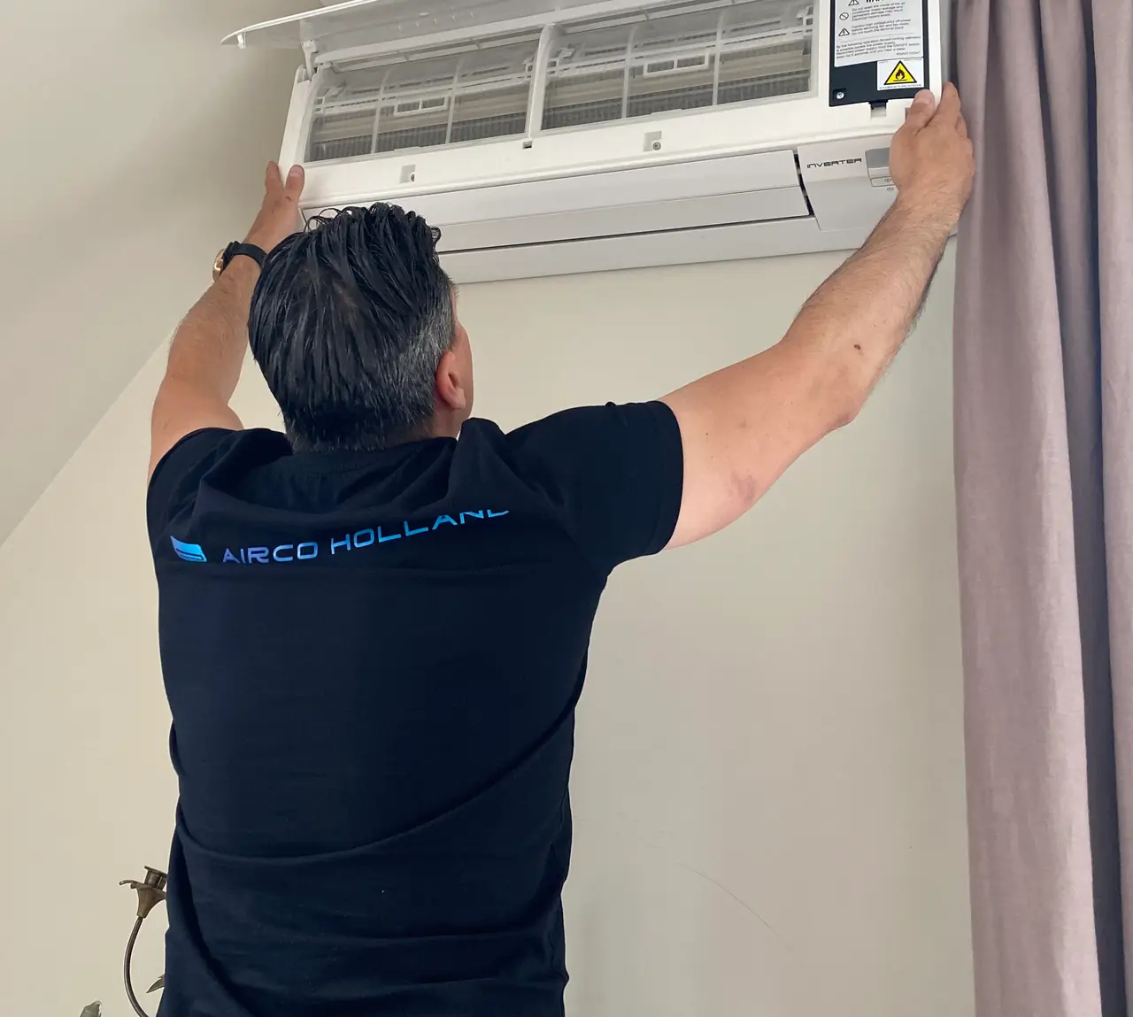 Een monteur van Airco Holland bij een wandmodel met de voorkap open en de filters in zicht.