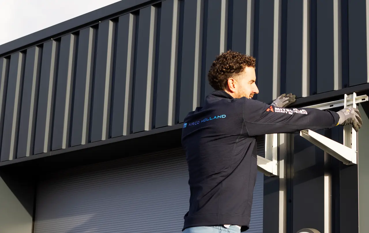 Rein positions a wall bracket for an outdoor unit on the dark wall of a business building.