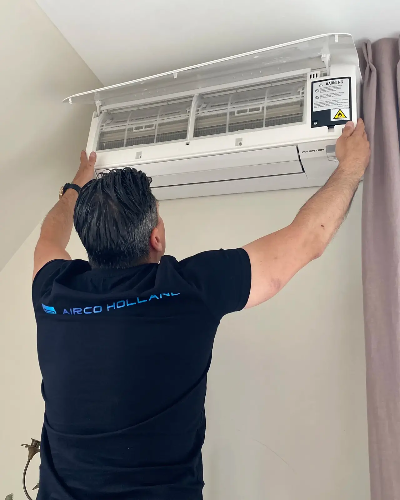 Een monteur van Airco Holland bij een wandmodel met de voorkap open en de filters in zicht.