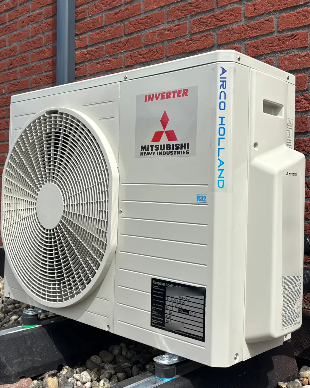 Buitendeel van Mitsubishi Heavy Industries met een R32-sticker en de zwarte kenplaat, tegen een bakstenen gevel.
