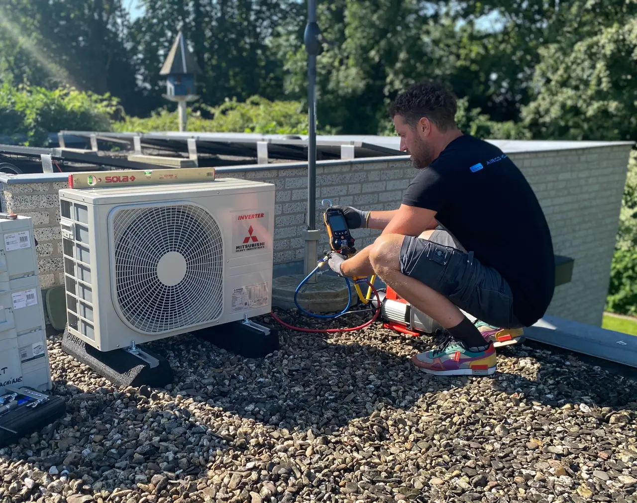 Rein meet met een digitale meter aan een buitendeel op een grinddak, met de zon door de bomen.