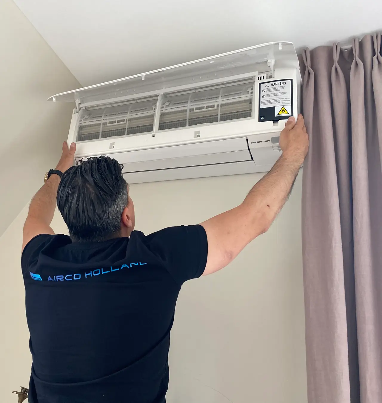 Een monteur van Airco Holland bij een wandmodel met de voorkap open en de filters in zicht.