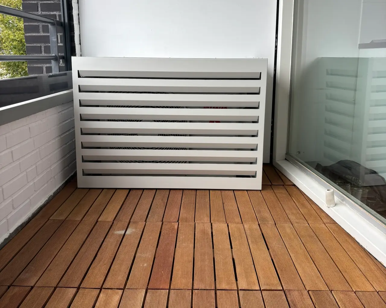 Een buitendeel in een witte lamellenkast op het balkon van een appartement, op een houten vloer.